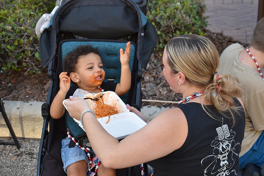 Ruskin's Jakoda Watson, 14 months, chows down on spaghetti from mom Chelsea Wood on the parade route.
