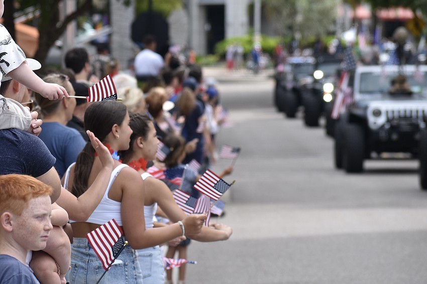 Parade attendees wave flags at the passing vehicles.