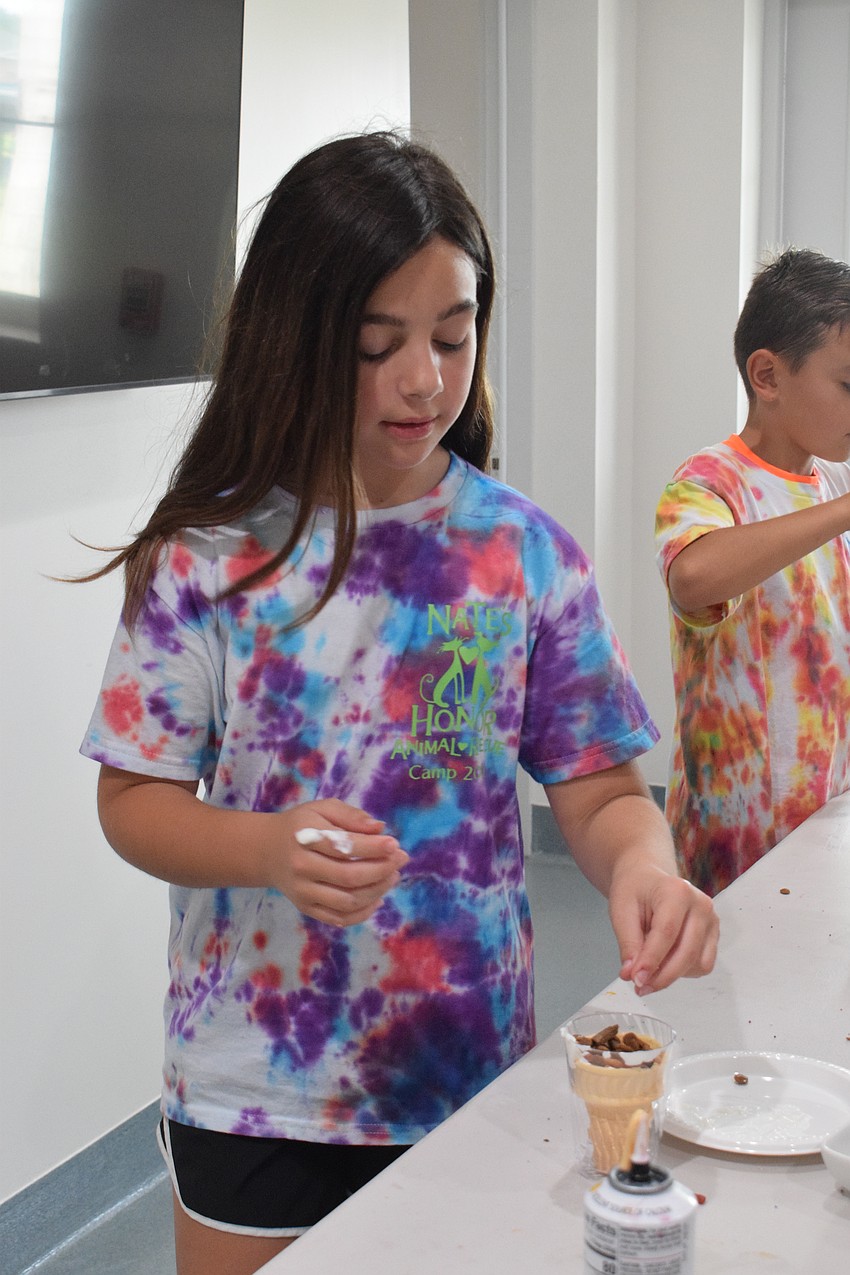 Aubrey Steward, who is 10, sprinkles dog treats into the sundae she's making for Nate's Honor Animal Rescue dogs. She hopes her sundae goes to Lux, one of the dogs she's spent time with at camp.