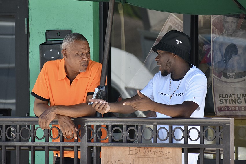 Ernso Joseph talks with Charlemagne Fenelon as they watch the event from the patio of Community Family Restaurant where they both work.