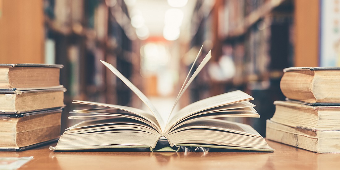 Book in library with old open textbook, stack piles of literature text archive on reading desk, and aisle of bookshelves in school study class room background for academic education learning concept