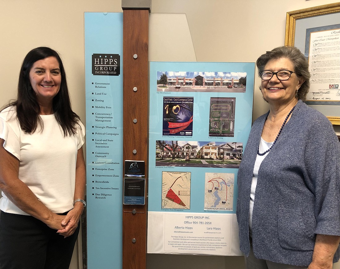 From left, Lara Hipps, vice president of Hipps Group Inc., and Alberta Hipps, president, stand next to a display at their West Jacksonville office listing their firm’s services.