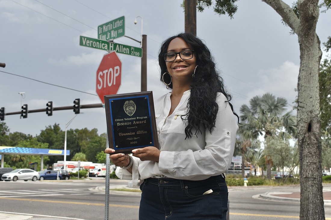Ronnique Hawkins stands at the road named in her mother's honor while holding an award received by Veronica Allen.