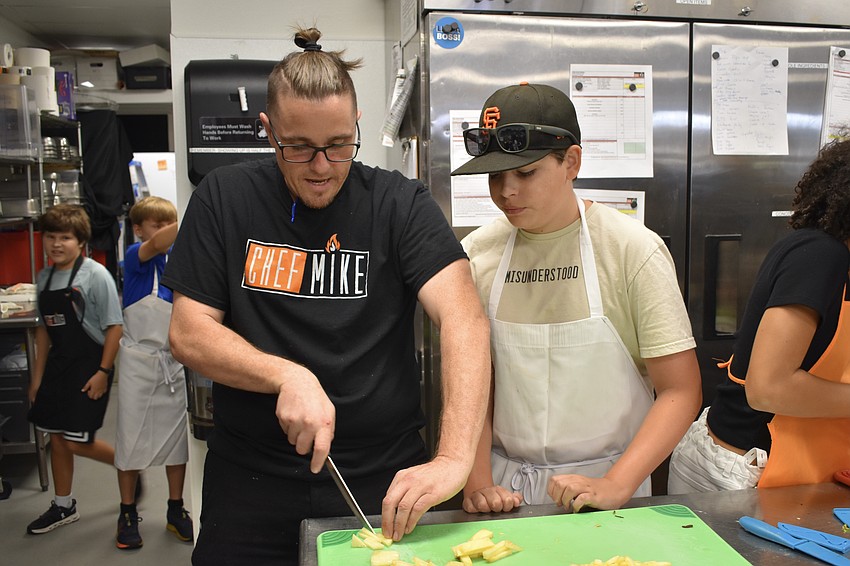 Mike Donnerstag shows 13-year-old Alexander Edwards how to slice the pineapple properly.