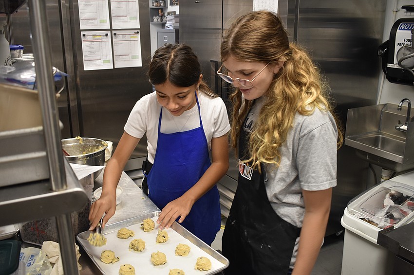 Zuleika Zuns, 12, and 13-year-old Kambryn Mira place the chocolate chip cookie dough they made on a baking sheet.