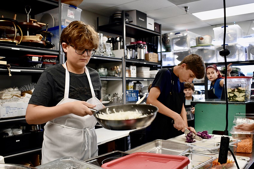 Saul Suarez, 13, cooks onions while and 14-year-old Jack Greenwell slices cabbage.