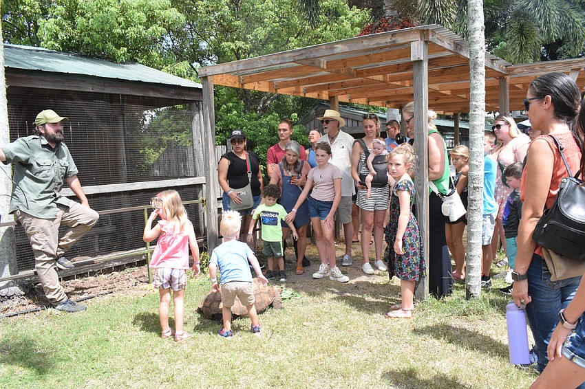 People listen as Damen Hurd, the president of Wild World Rescue, share facts about Speedy, a tortoise.