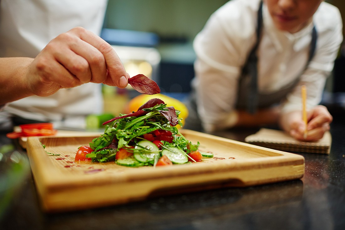 A chef places a leaf of basil on top of a salad. Photo from Adobe Stock