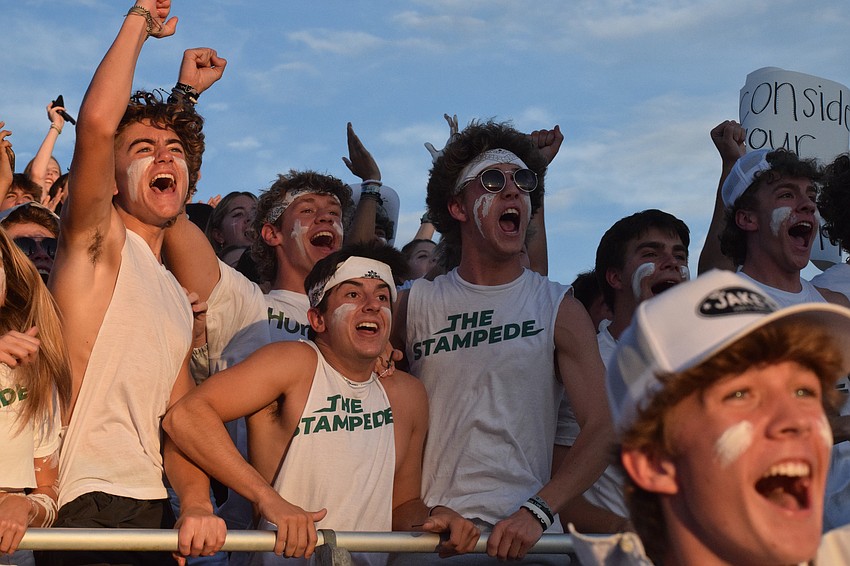 Lakewood Ranch High School juniors Ledge Newton and Carson Wozniak and senior Ryan Donnelly jump up and down and cheer as the football team scores a touchdown.