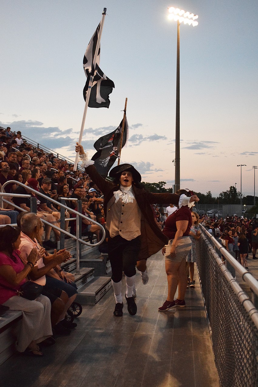 Braden River High School senior Alex den Boggende runs through the stands with a school flag in celebration of the football team scoring a touchdown.