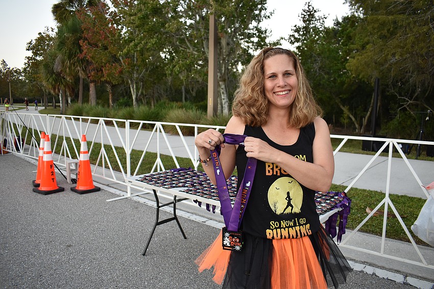 Lakewood Ranch Running Club volunteer Christine Rouse gives out medals at the finish line. Her shirt says, 