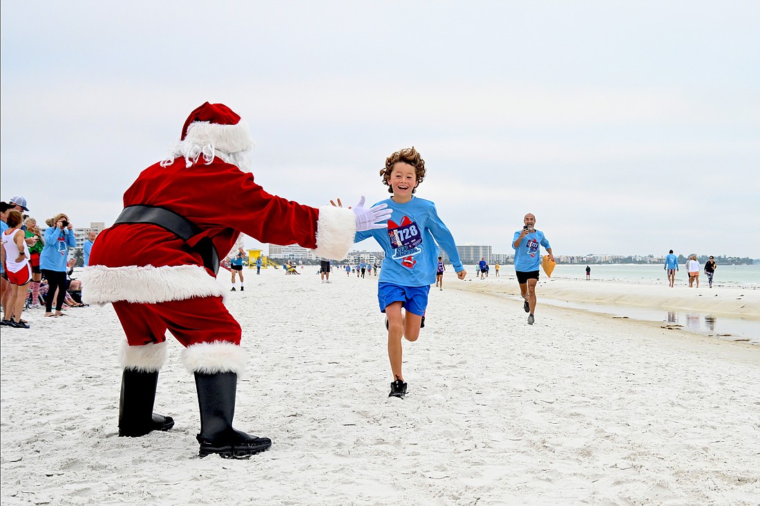 Santa greets a young runner at the finish of the 2022 Sandy Claws Beach Run.