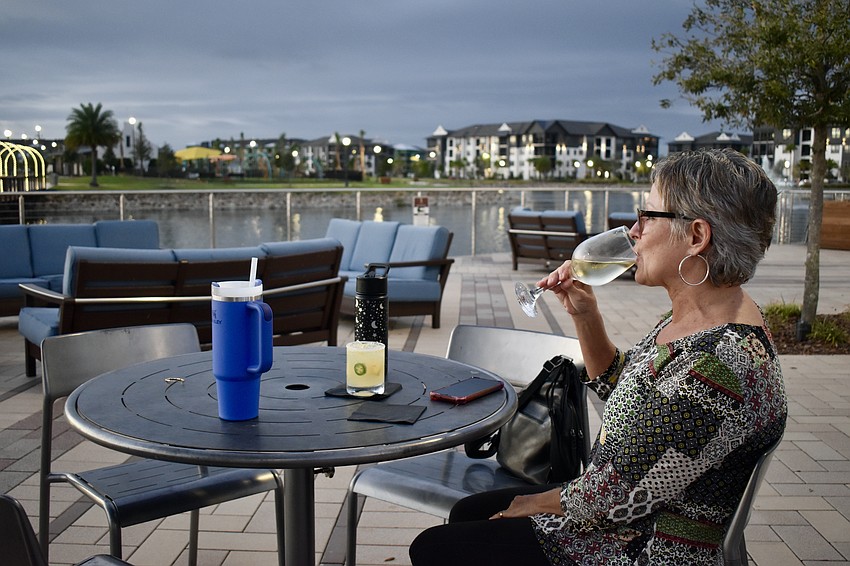Lakewood Ranch resident Krista Aquino enjoys the Sights and Sounds series with a glass of wine at Waterside Place while her family plays across the bridge at the park.