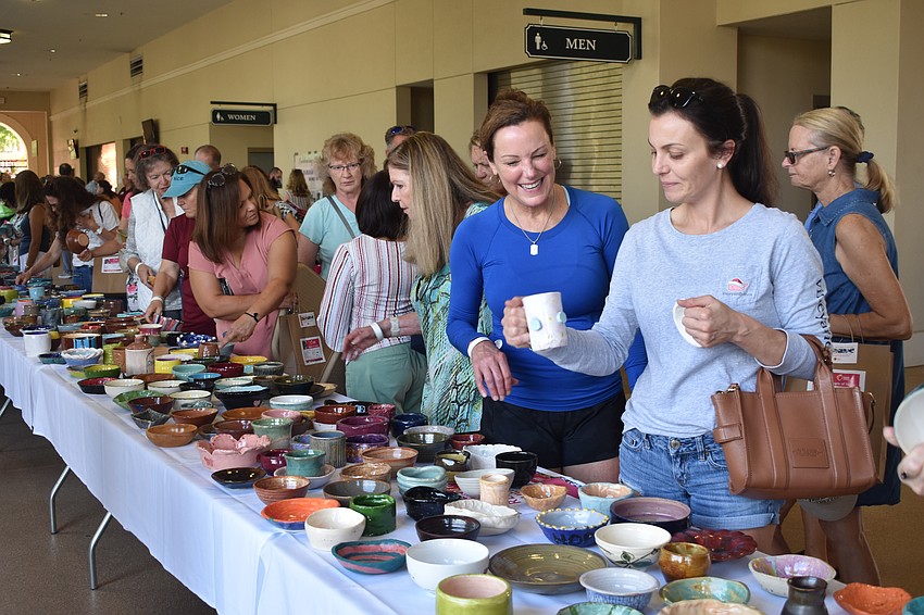 Attendees line up along the table of pottery, with Valerie Lindsey and Brittany Boron at the right.