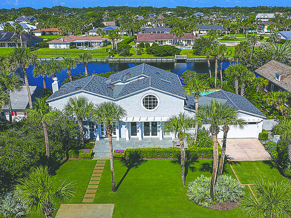 Lakefront coastal design two-story home features three bedrooms, four bathrooms, porches, patio, balcony pool and dock.