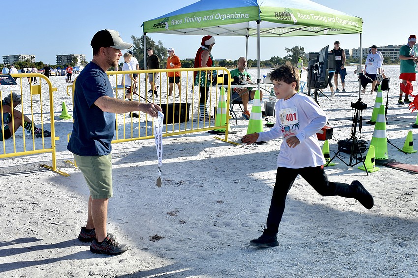 Scott Moranda holds out a medal for Nico Skuba, 8, at the finish line of the 5K.
