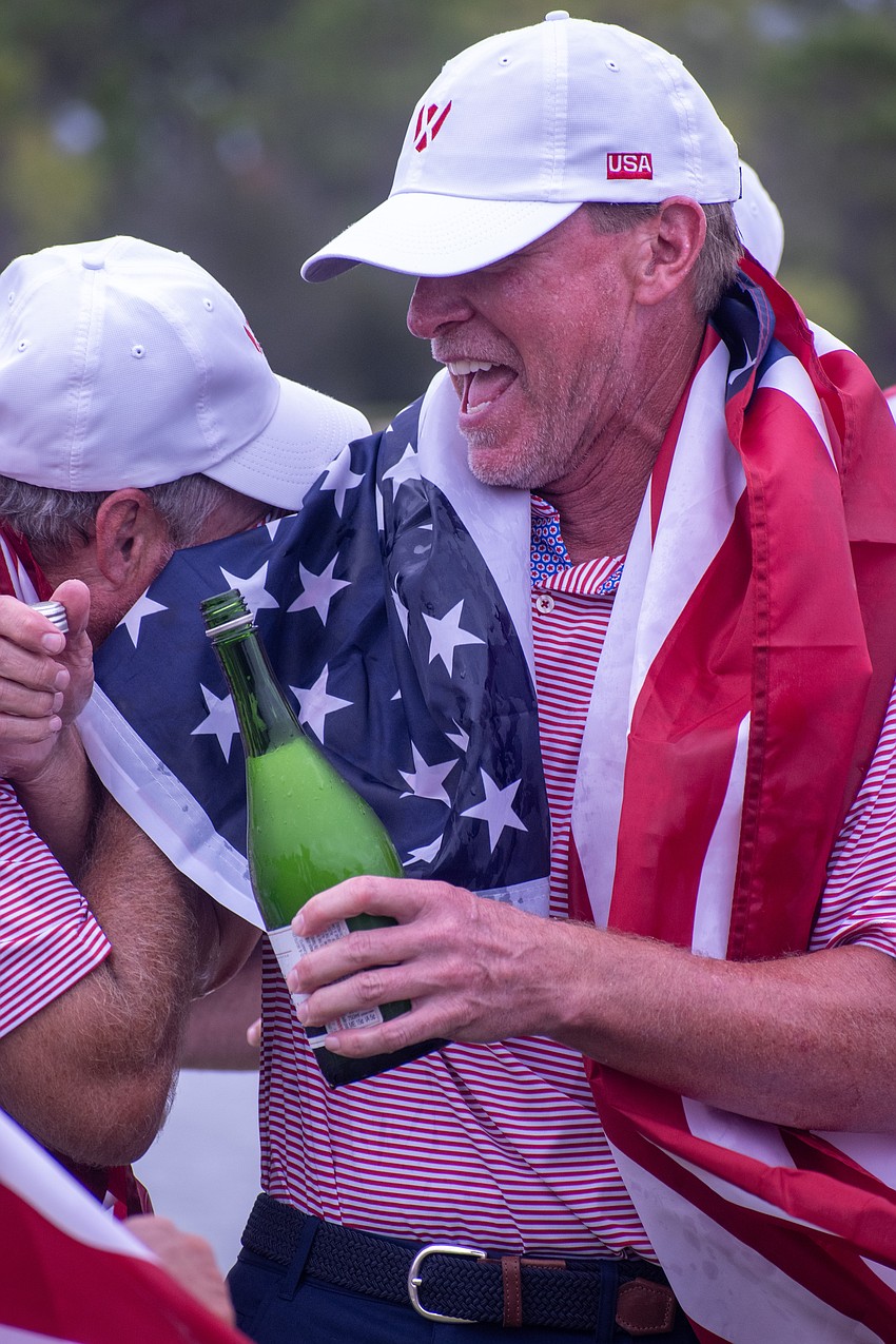 Jerry Kelly wipes champagne from his eyes via Steve Stricker's American flag as Stricker laughs. The pair helped Team USA win the first-ever World Champions Cup, held at The Concession Golf Club.