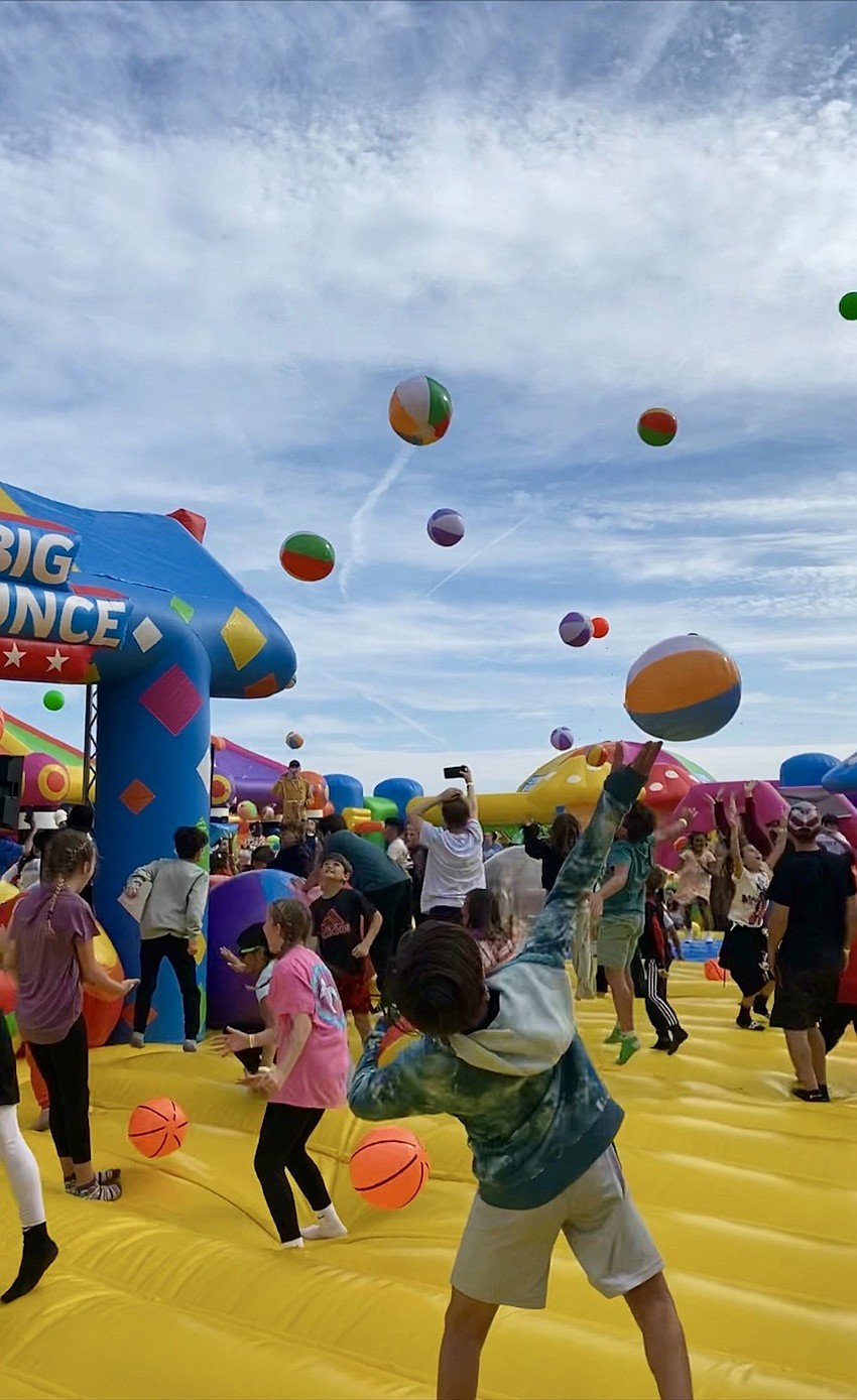 Kids are throwing beach balls in the air and at their parents. The DJ incited a kids versus parents dodge ball war.