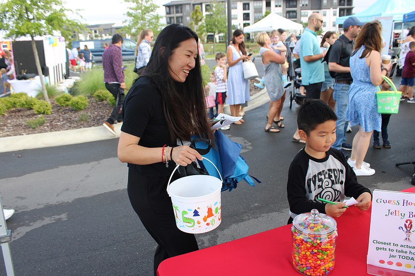 Abby Zou watches as her son, 6-year-old Orson Li, makes his guess at the number of jelly beans in the jar in an East County Observer game at Eggstravaganza.