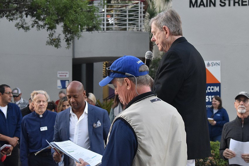 Chaplain Tom Pfaff, City Commissioner Kyle Battie, Men of the Redeemer leader Craig Burness stand by as County Commissioner Mark Smith speaks at the first station.
