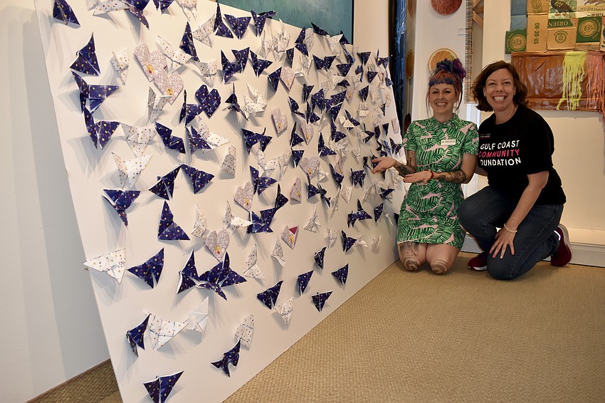 Megan Howell and Jennifer Johnston stand beside an oragami collage created by guests at the event.
