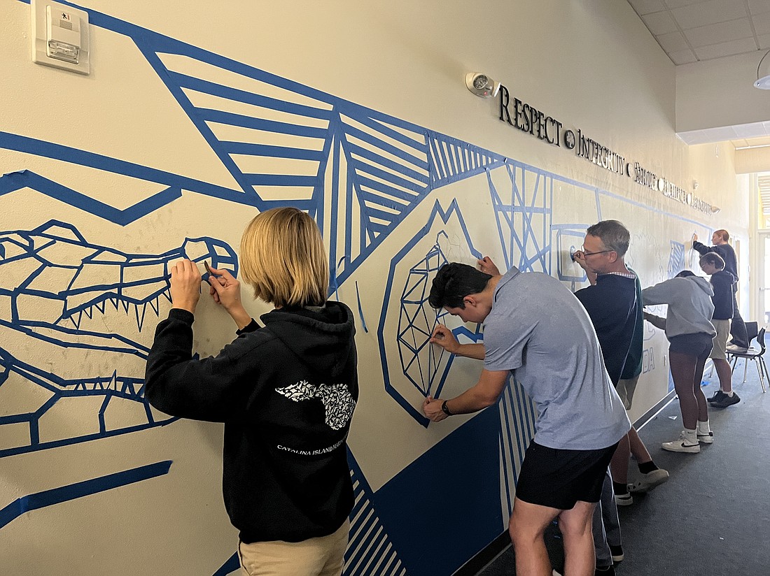 The Out-of-Door Academy upper school students and staff work on a tape mural featuring the mascots of the school's house system.