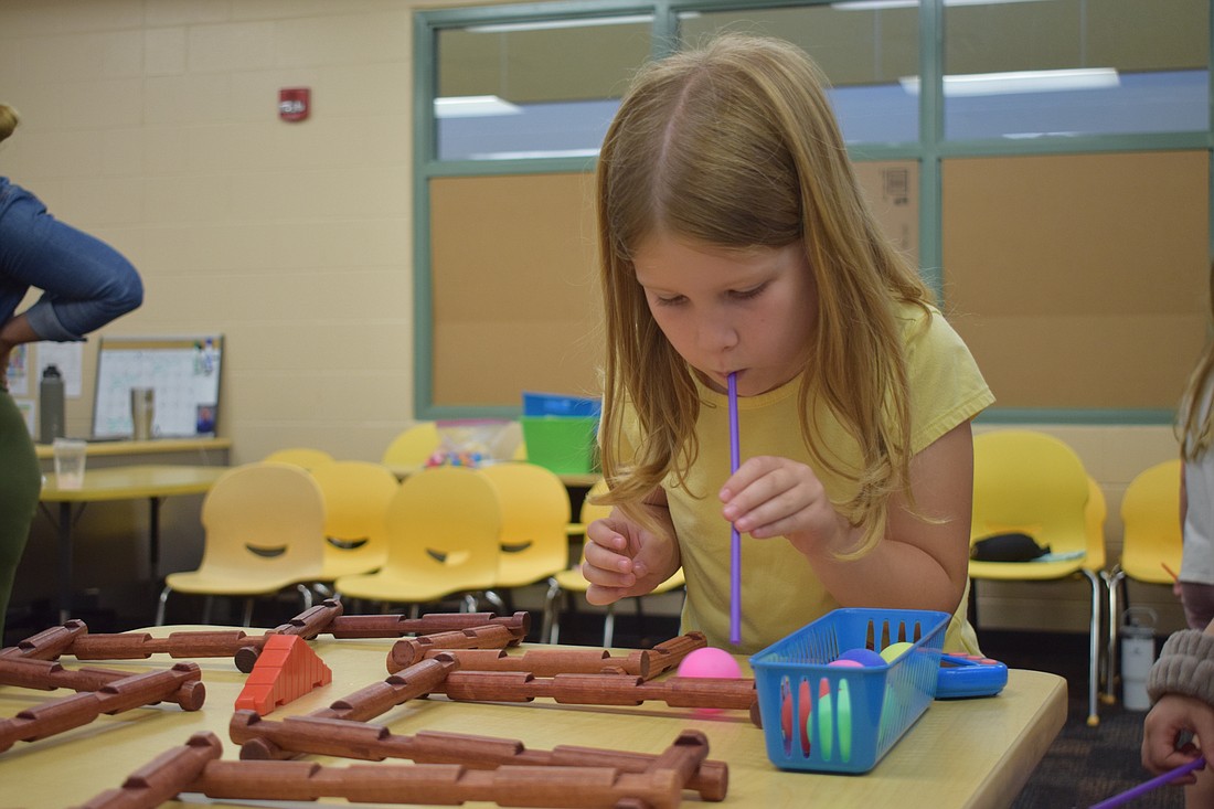 First grader Anna Lum blows a ball through a maze at the wind powered maze activity.