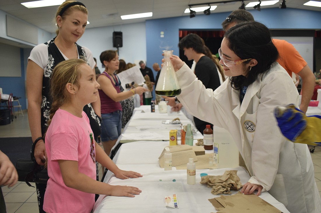 Elena Bubnova and her daughter, second-grader Milana Bubnova, help Meily Fernandez perform a science experiment at the table of Sarasota High School's MaST Research Institute.