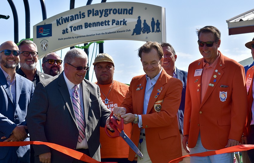 Past and current Kiwanis presidents Neil Unruh and Andy Minor cut the ribbon on the playground as they're surrounded by Kiwanis members and county commissioners.