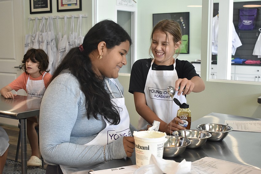 Delaney Saldivar, 12 and Ember Magnuson, 11, drip honey into a bowl as they build a red, white and blue smoothie.