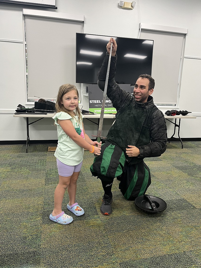 Peyton Swartz, who is 6, has her chance to hold a long sword with the help of Chris Fontana, a junior instructor with Steel Ring Academy. Swartz says she loved watching the live sword fighting demonstrations.