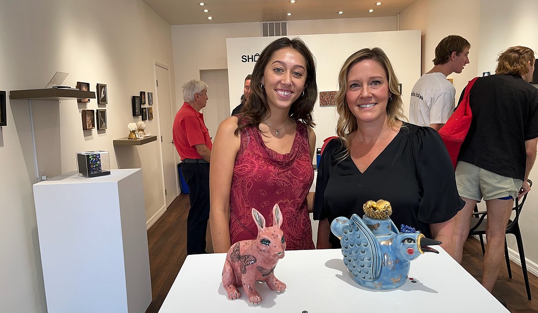 502 Gallery Operations Manager Christina Antoniou and co-owner Cassia Kite pose in front of some of the small pieces featured in the "Shopliftable" show.