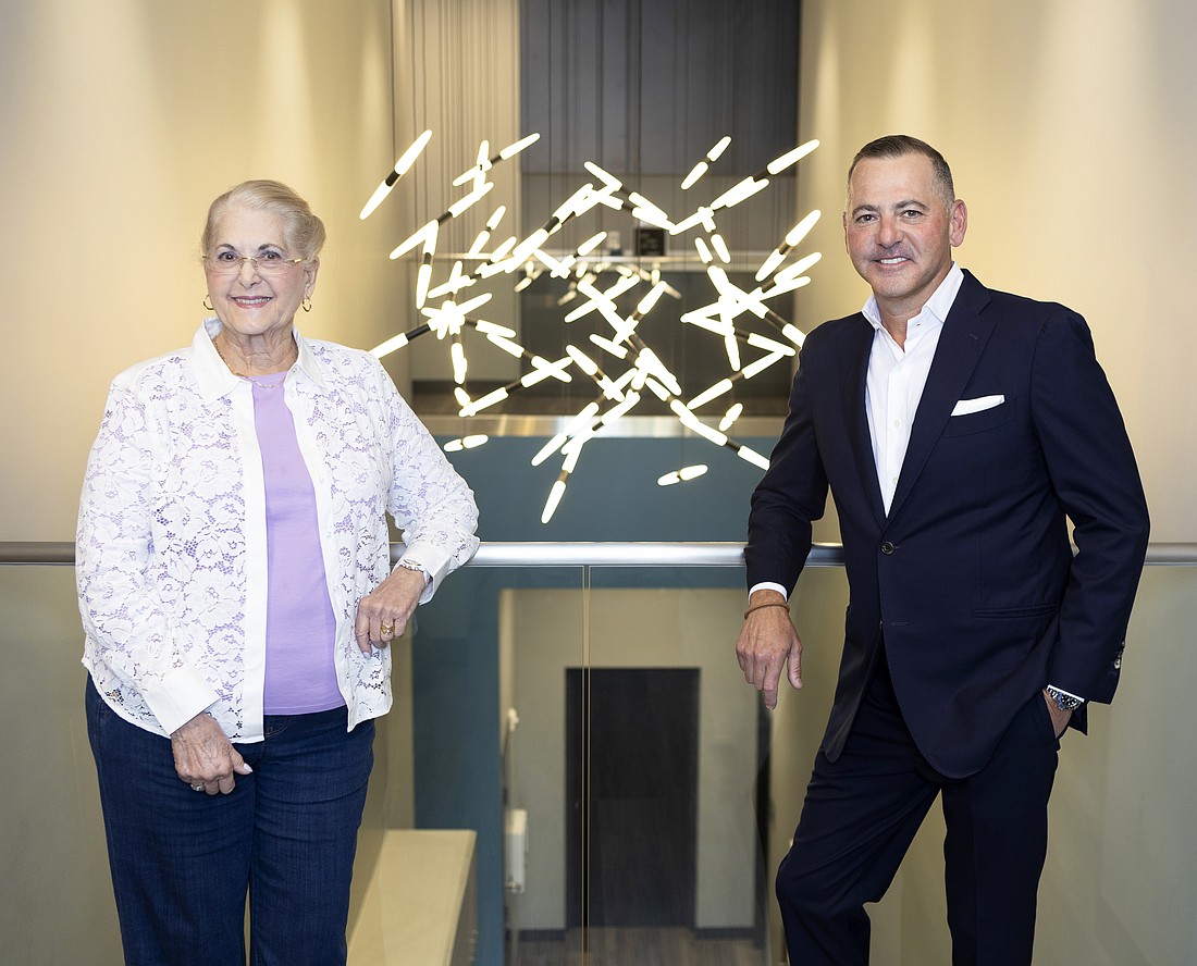 Lynne Merriam, founder of Clinical Research of West Florida and Aydin Keskiner, CEO of CRWF pose in front of a molecular sculpture above the atrium of the Tampa location.