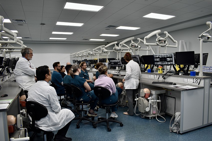 A group of LECOM students are in the middle of class as the alliance tours the simulation lab.