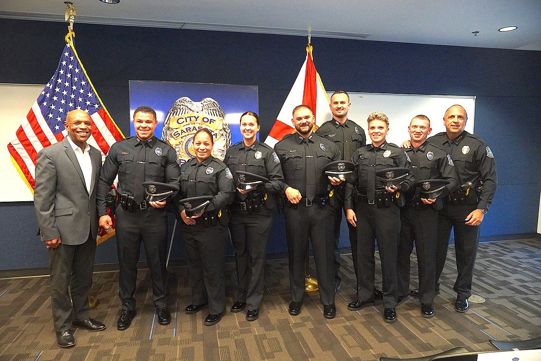 The seven new SPD officers are flanked by Sarasota City Manager Maron Brown (left) and Chief Rex Troche (right).