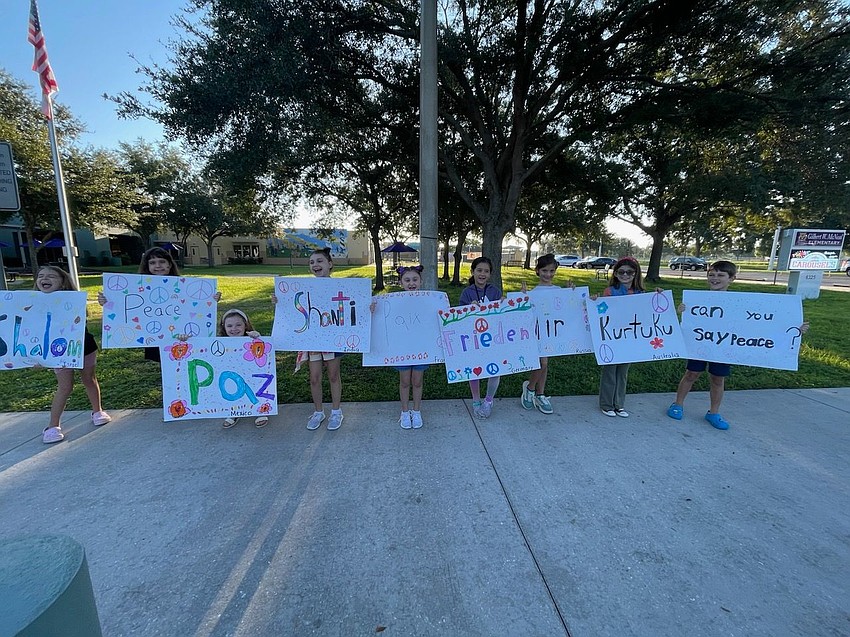 Students line the walkway leading to Gilbert W. McNeal Elementary School holding signs saying 