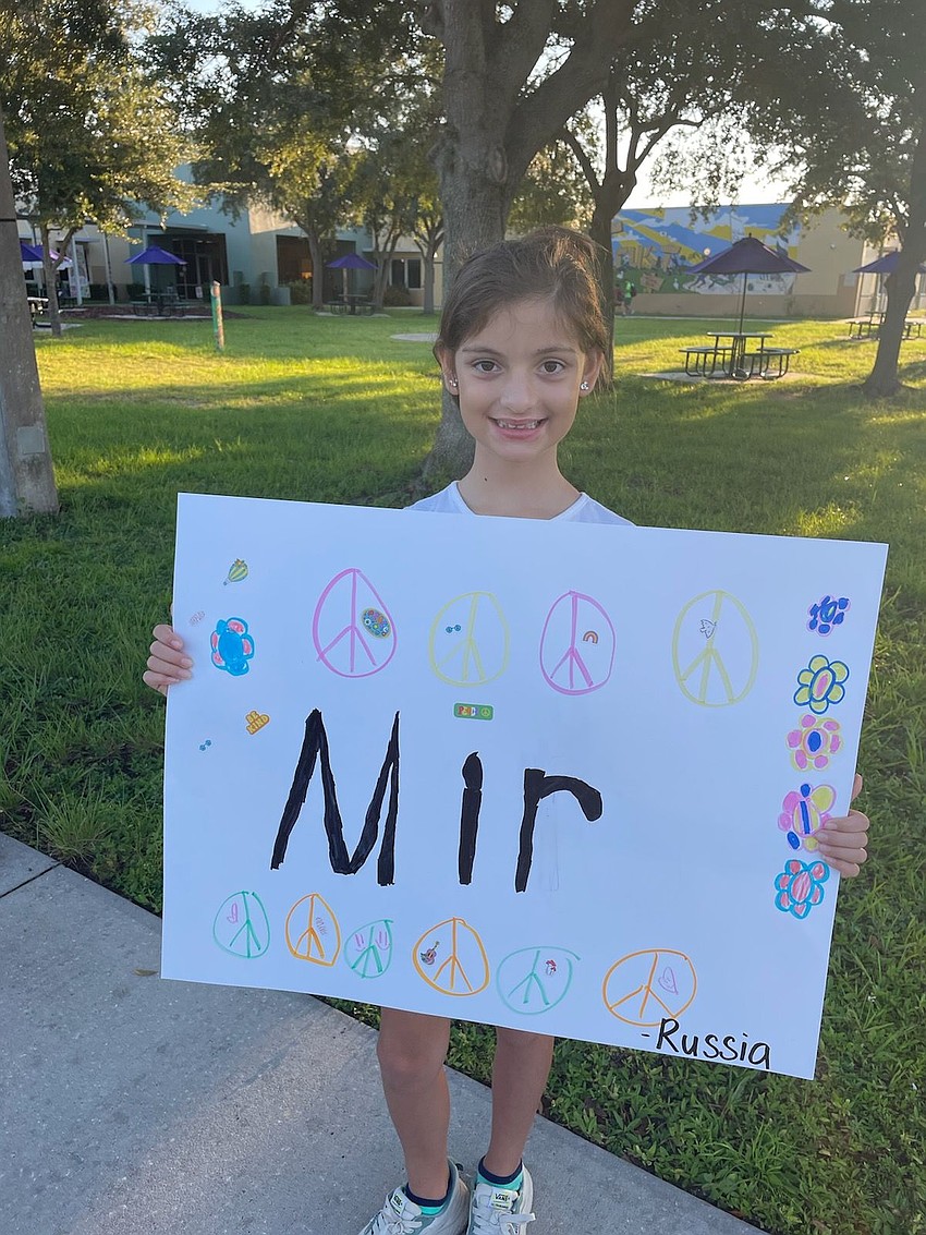 Maia Vergnais greets students by holding up a sign that shares how people in Russia say 