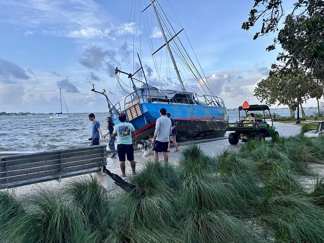 Passersby stop to look at a large sailboat that lies beached on Bayfront Park on Friday, Sept. 27, a day after Hurricane Helene passed through the area.