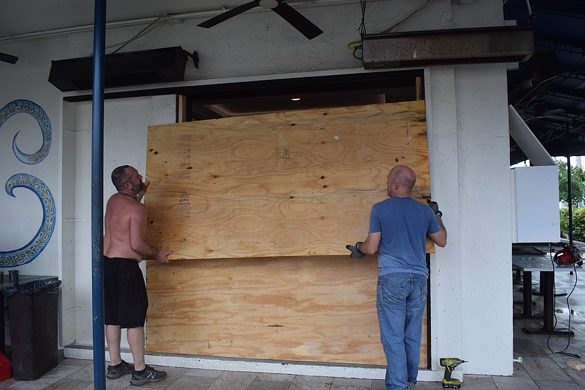 Crab and Fin employees Troy Forman and Chris Coehler boarding up the broken window after Hurricane Helene.