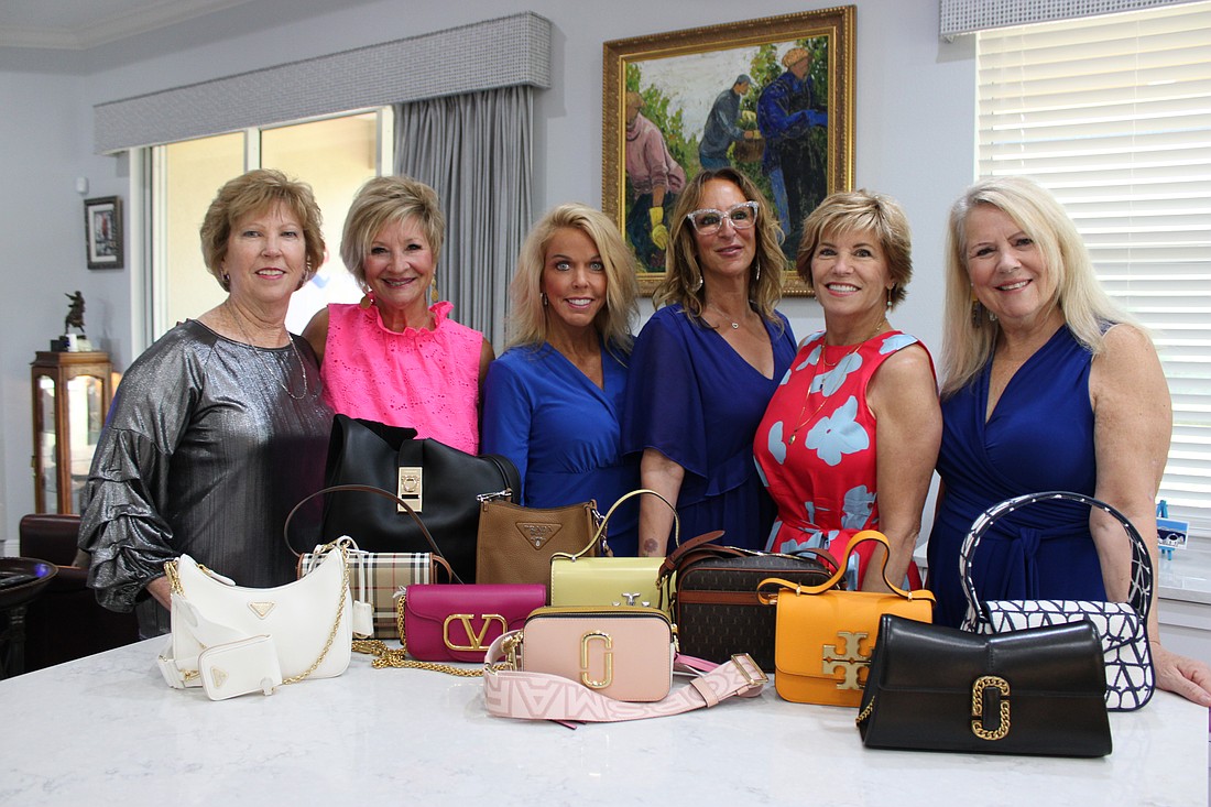 Sisterhood for Good members Kathy Collums, Maria MacDonald, Julie Benjamin, Samina Morrow, Angela Massaro-Fain and Becca Towery stand in front of the designer handbags that will be up for grabs during Designer Bag Bingo Oct. 10.