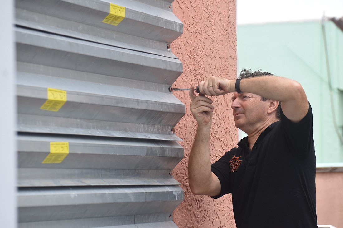 Thierry Raynal, owner of Bonjour French Cafe, fastens a covering to a window at Bonjour French Cafe.