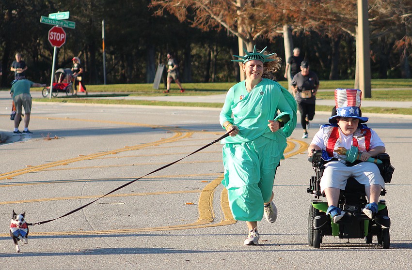 Panda the dog races along the Boo Run route with Monika Oberer and Grayson Tullio, who dressed as the Statue of Liberty and Uncle Sam to remind people to vote on Election Day.