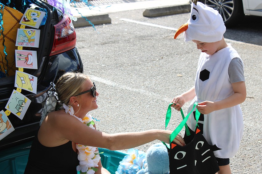 Hailey Hodges mans a trunk or treat post, handing out candy to Kiddie Academy student William Johnstone during the parade at the school.