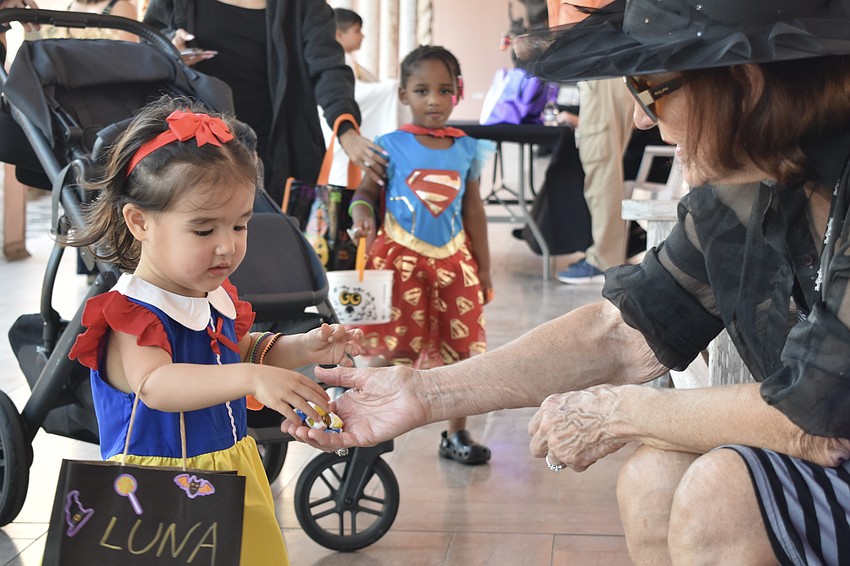 Luna Chin, 2, and Nyla Jones, 3, stop at a station, where Lynda Wright is helping to hand out treats.