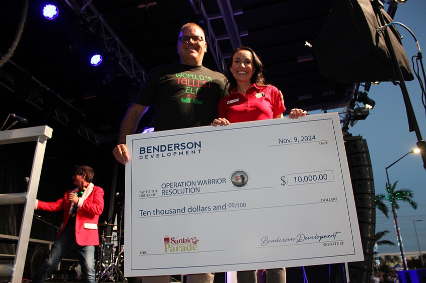 Benderson Development's Todd Mathis presents Operation Warrior Resolution CEO Kendra Simpkins with a check for $10,000 to honor veterans before the Santa's Grand Arrival Parade.