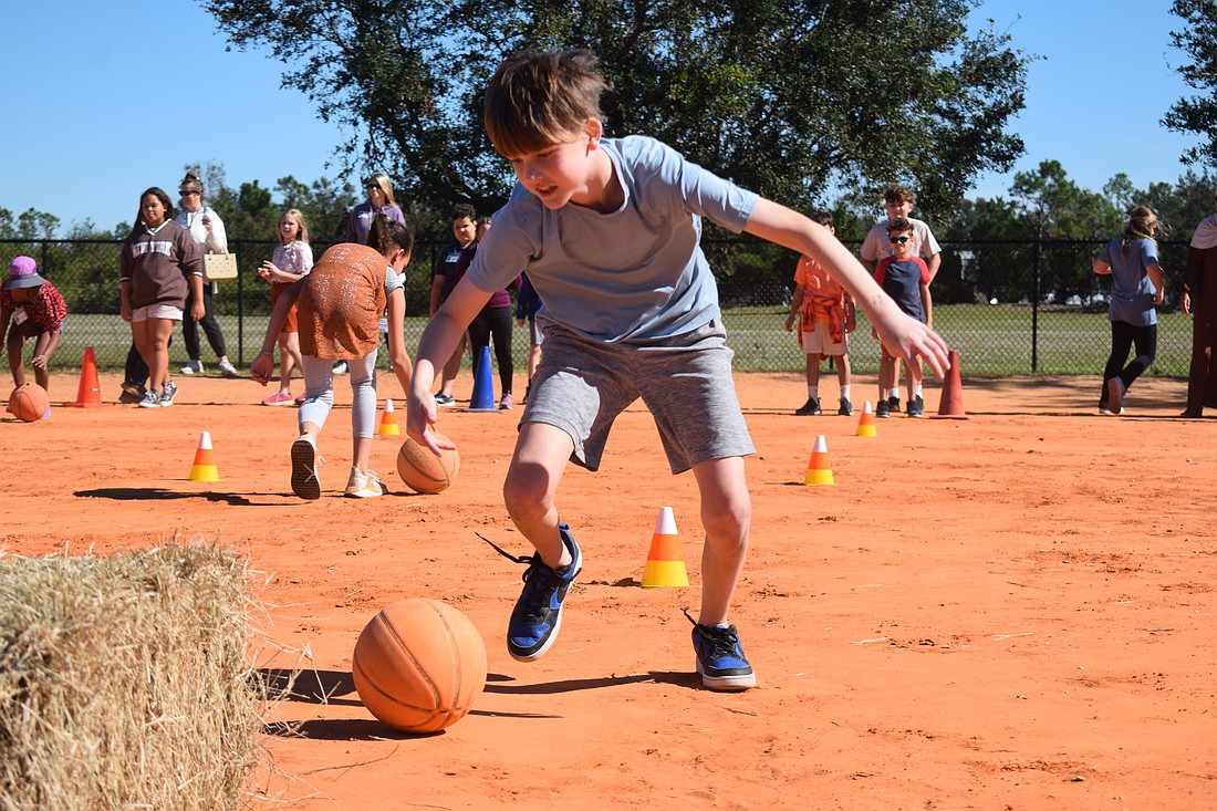 Fifth grader Grayson Hermann pushes the basketball, meant to represent a pumpkin, through the cones to the hay and back as fast as he can.