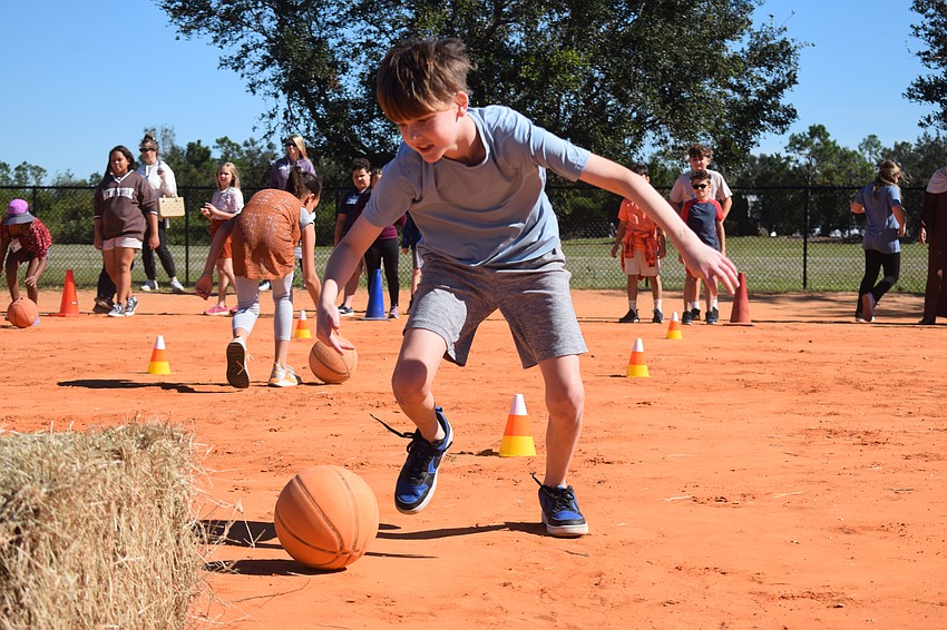Fifth grader Grayson Hermann pushes the basketball, meant to represent a pumpkin, through the cones to the hay and back as fast as he can.