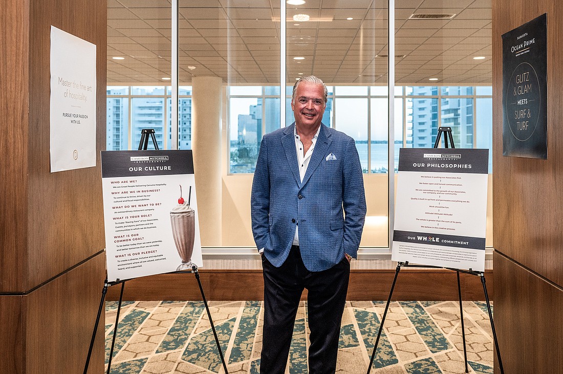 Cameron Mitchell, CEO of Cameron Mitchell Restaurants, stands next to posters detailing his company's values and philosophy at employee training in Sarasota.