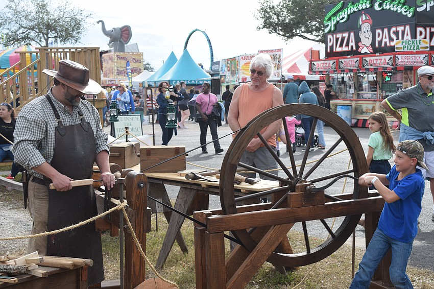Keaton Winget lends a hand to Trenton Tye, owner of Purgatory Ironworks, during a blacksmith demonstration at the Manatee County Fair Saturday.