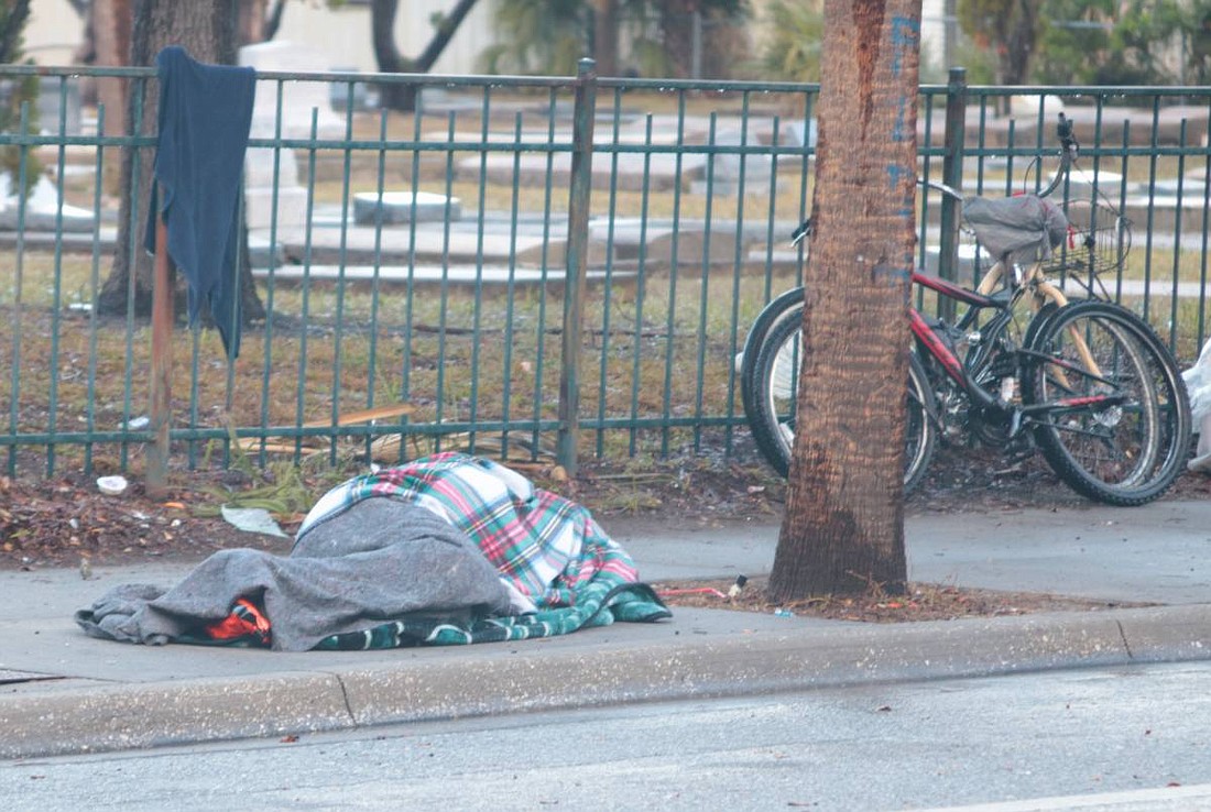 A person bundled against the cold and rain lies on the sidewalk across the street from the Salvation Army in Sarasota Wednesday, Jan. 22. The county is working with the organization to open a cold weather shelter for the next two nights.